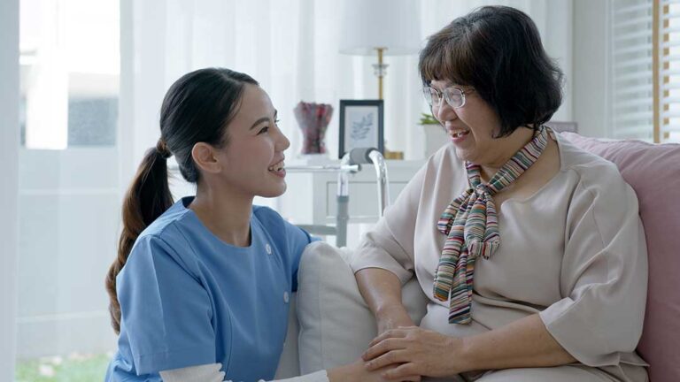 An older adult unpacks family photos with a visiting loved one in a bright, home-like room.